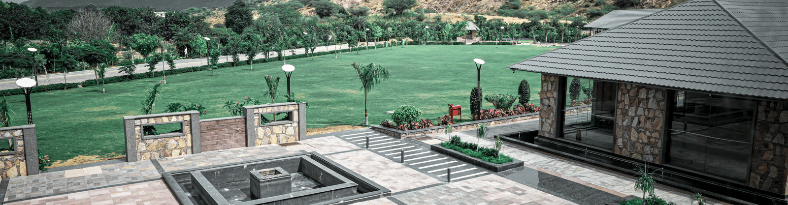 A large, curved swimming pool at a holiday resort. It's surrounded by wooden decking and a backdrop of buildings and green hills.