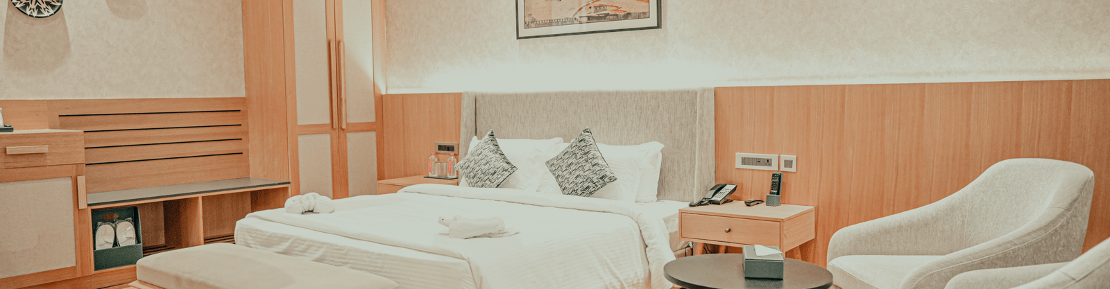 A luxurious hotel room with a large, neatly made bed, a bench at the foot of the bed, and an armchair next to a round table.