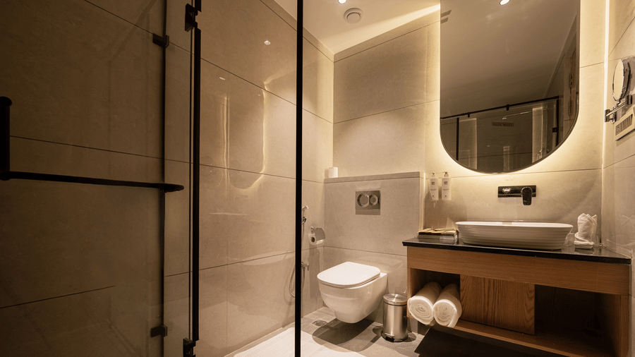 A clean bathroom vanity area with a white vessel washbasin and a large round mirror with backlighting at Ananta Express, Katra.