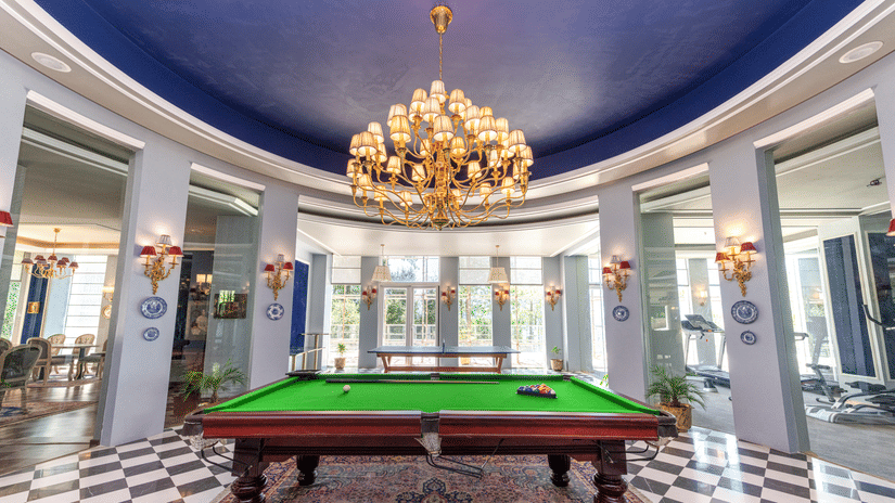 Elegant game room at The Manor Wellness & Sports Hotel - stunning blue ceiling, golden chandelier & professional snooker table in grand circular space.