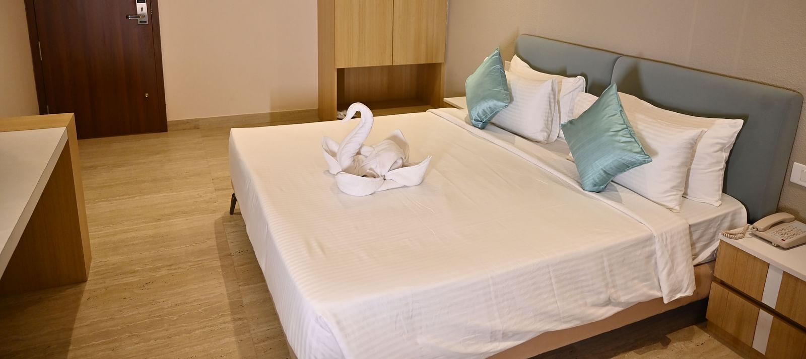 A well-lit hotel room with a neatly made bed, a wardrobe, and a wooden door along with swan-shaped towels adorn the bed at TGI Livancia Hillside
