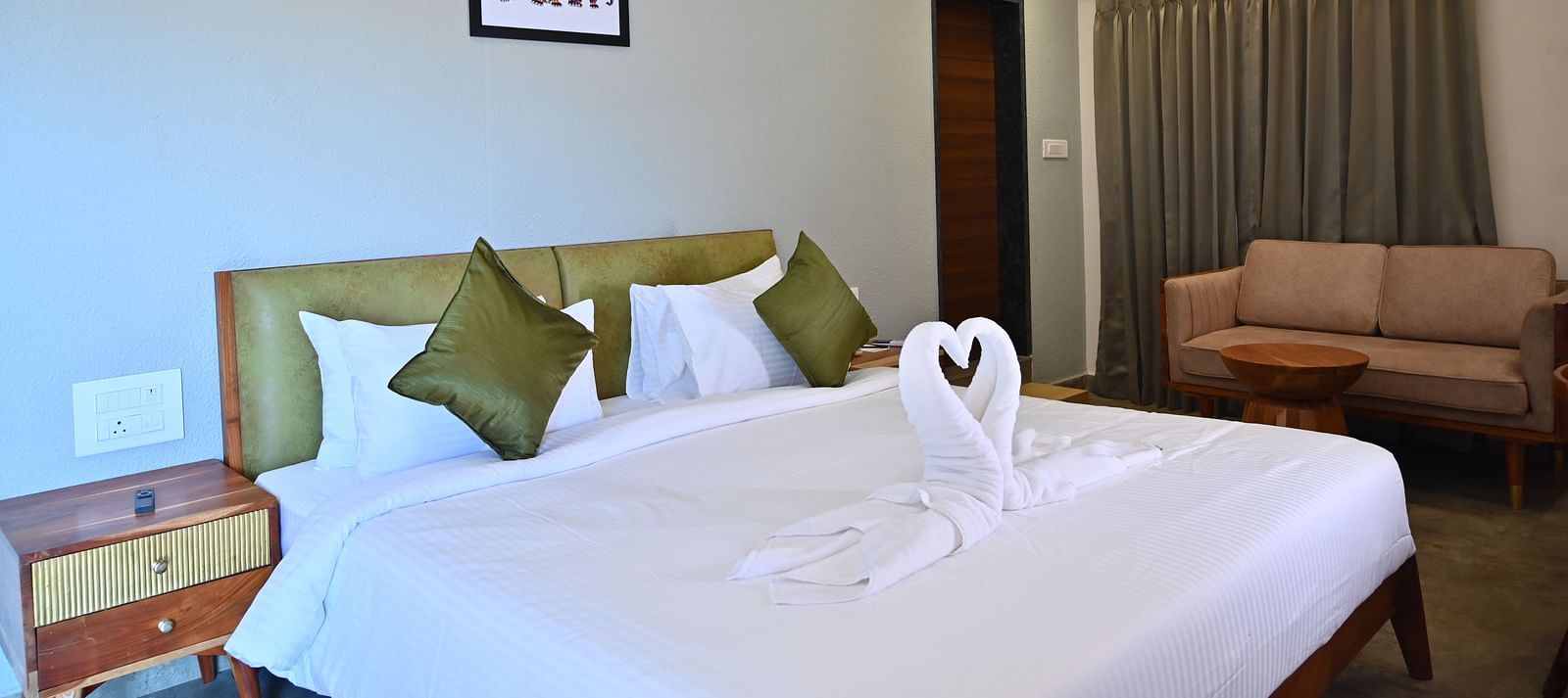 Club Suite featuring a large bed with pillows, a towel swan, a sofa, and warm wooden furniture at TGI Livancia Hillside