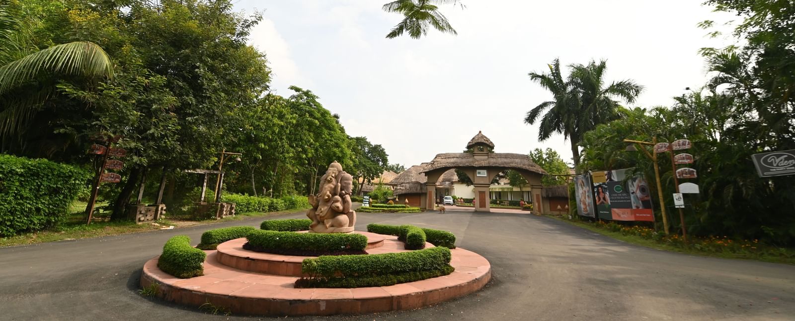 A landscaped garden path leads towards a distant building or structure, surrounded by trees and manicured bushes | Vedic Village Spa Resort, Kolkata