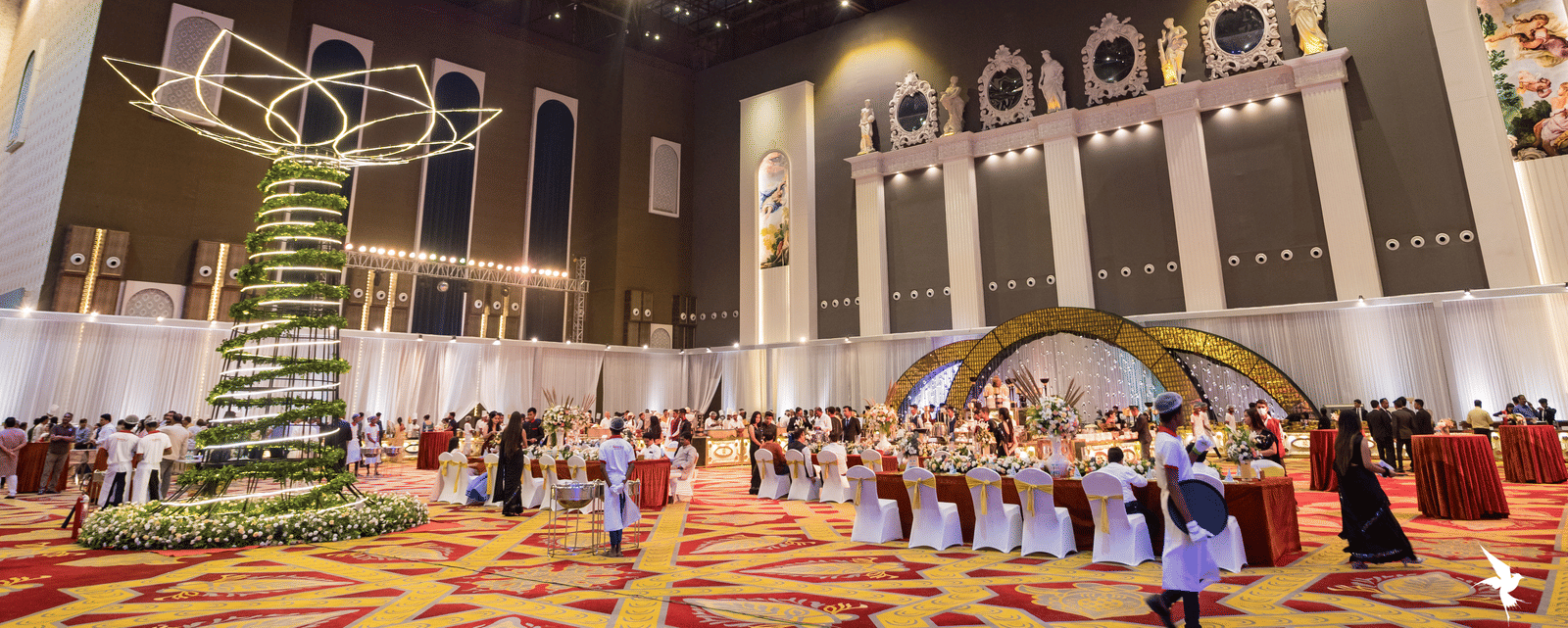 Vast, high-ceilinged convention or banquet hall decorated for an event with a large hanging ornament and a crowd of people at Hotel Hukam's Lalit Mahal.