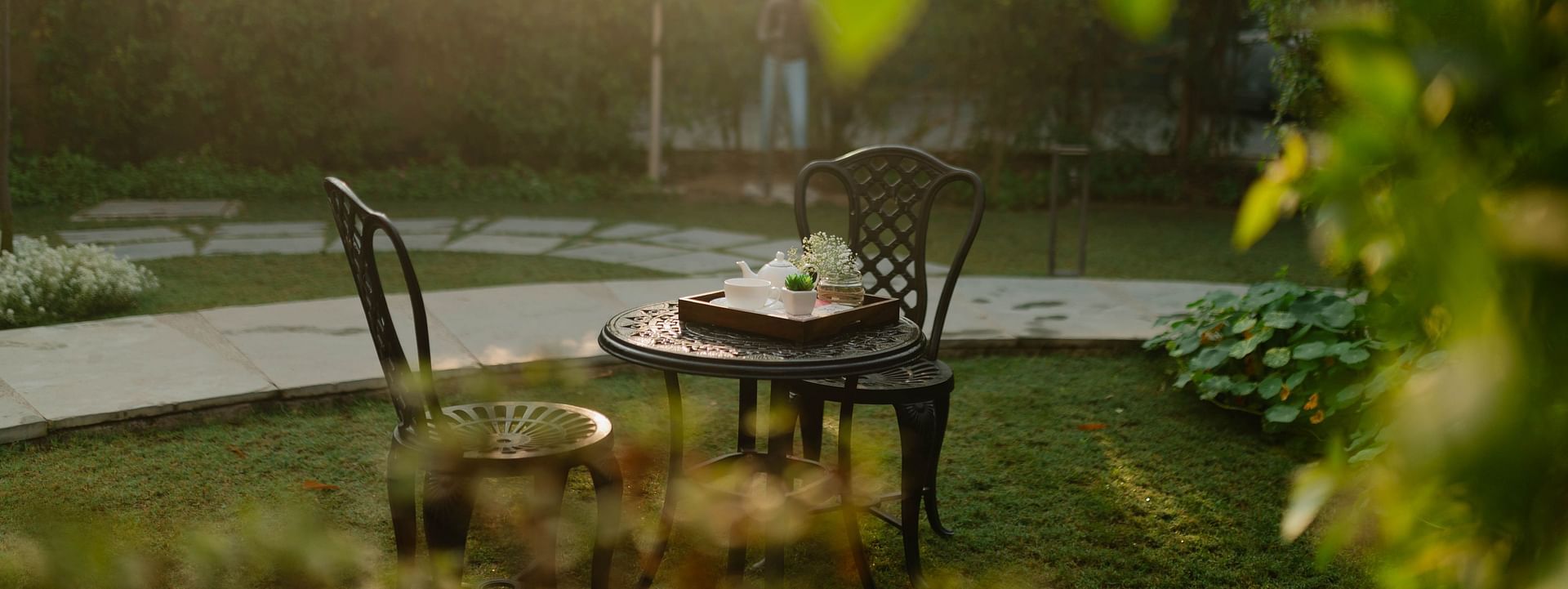 Outdoor seating at Karma Chalets with a round table near a water body and garden area during sunset.