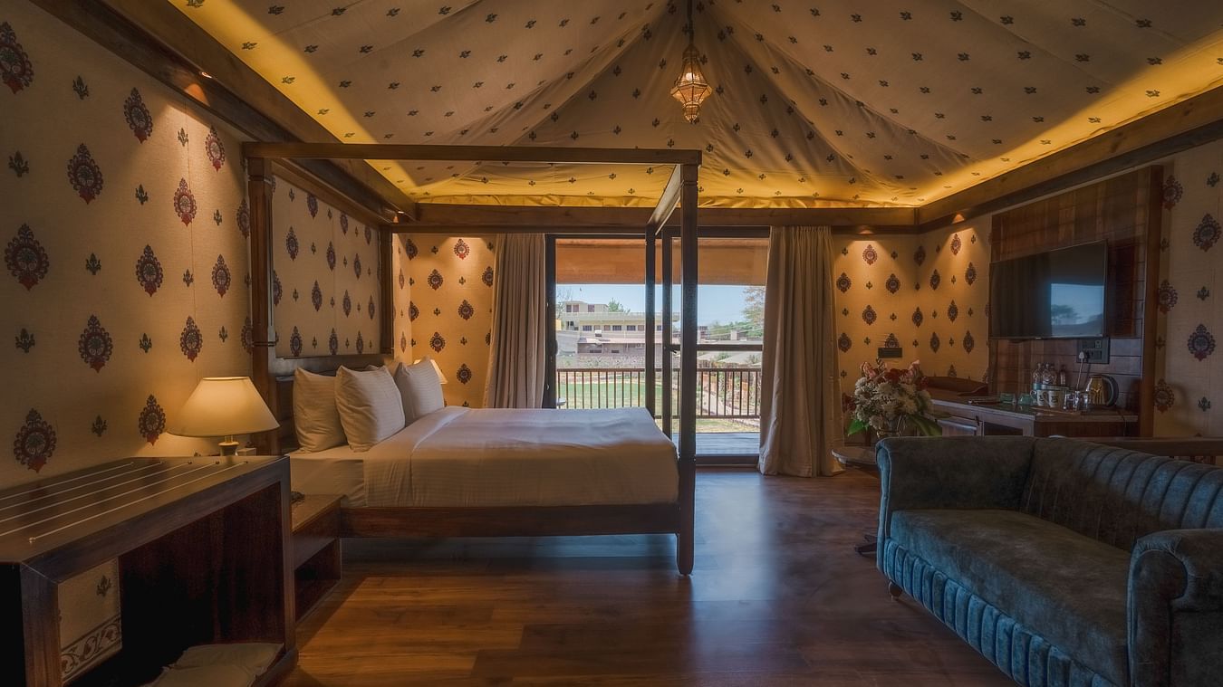 A Premium Duplex Tent featuring a poster bed, a sofa, a flat TV screen and a table beneath, a cabinet table, and a balcony attached at The Baagh Ananta Elite, Ranthambore