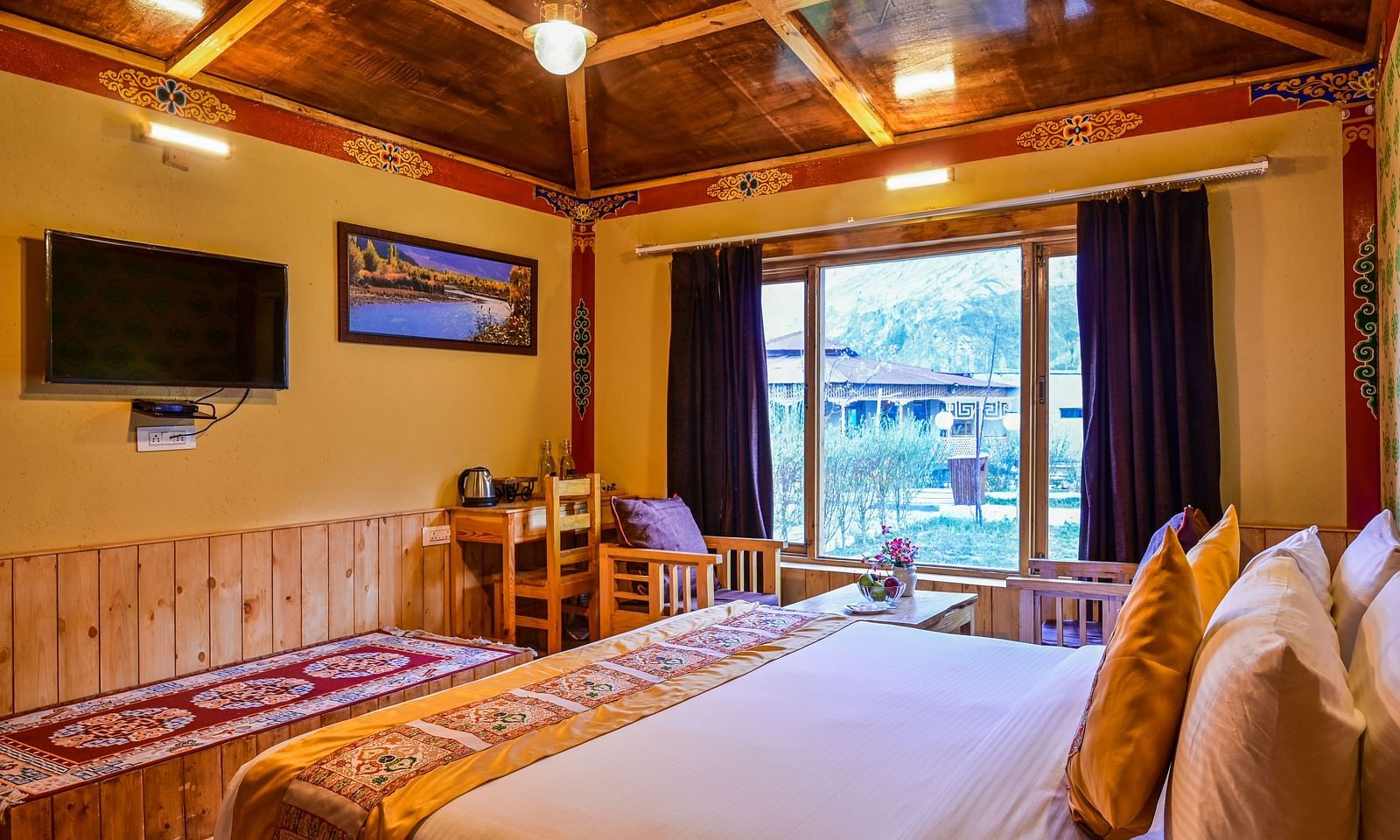 Premium Cottage at White Sands Resort, Ladakh features a king size bed with patterned linens, a seating area, and a view of the outdoors through a window.