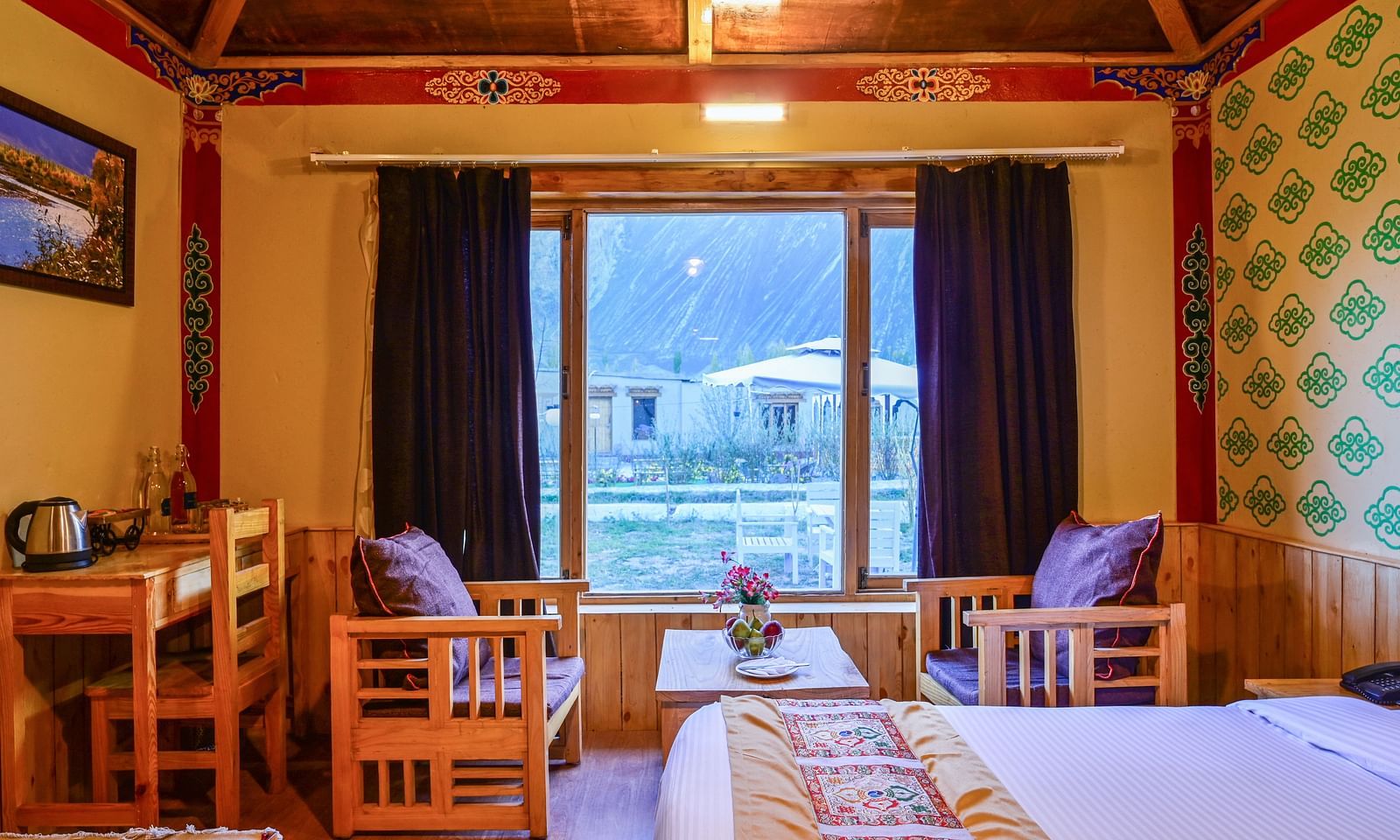 Premium Cottage at White Sands Resort, Ladakh, is furnished with a king size bed, a dining table, chairs, and vibrant wallpaper.