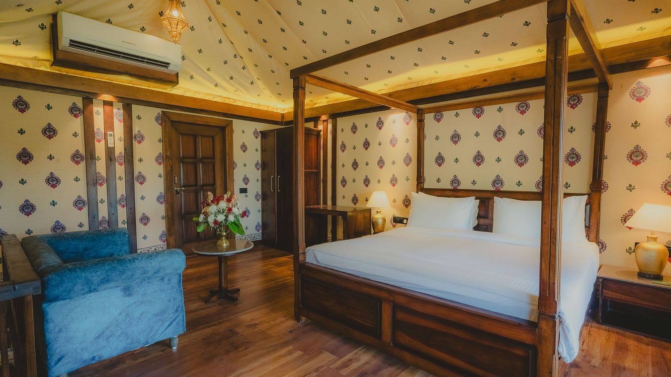 A Premium Duplex Tent bedroom featuring a sofa, a poster bed, bedside table with lamps on either side, cabinet table, a wardrobe, and a centre table with flower vase at The Baagh Ananta Elite, Ranthambore