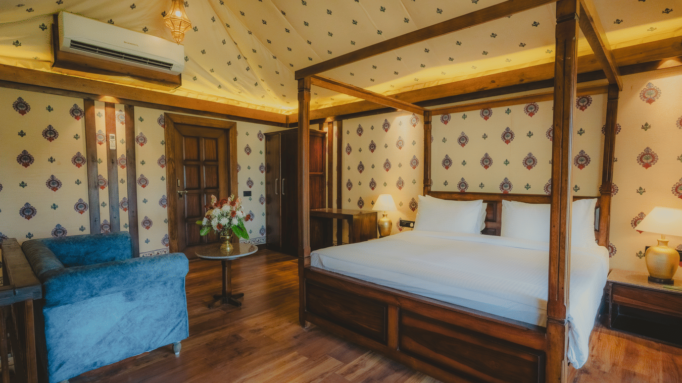 A Premium Duplex Tent bedroom featuring a sofa, a poster bed, bedside table with lamps on either side, cabinet table, a wardrobe, and a centre table with flower vase at The Baagh Ananta Elite, Ranthambore