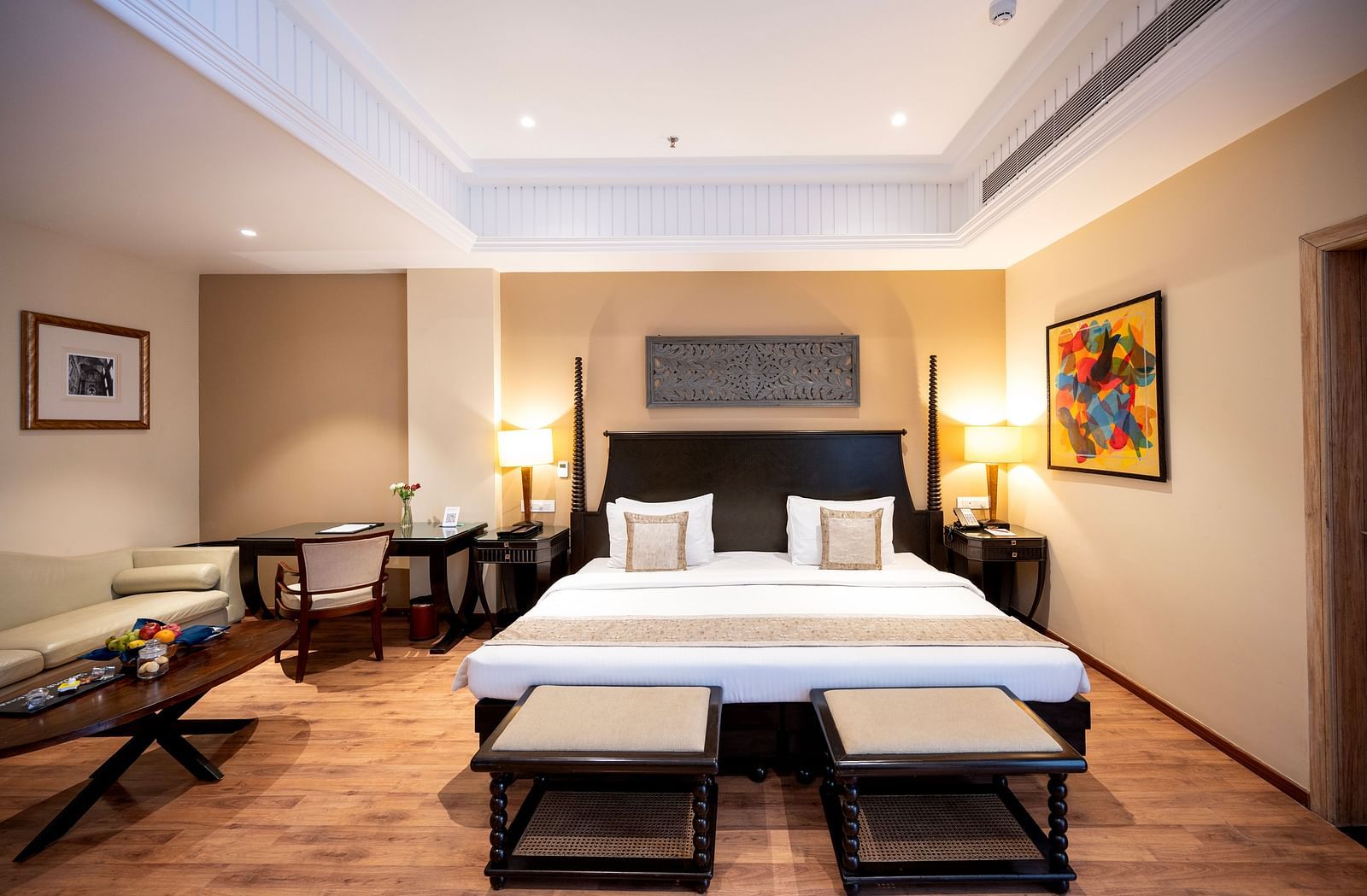 Presidential suite bedroom at Essentia Luxury Resort & Spa, Udaipur, featuring a neatly made bed, a side sofa seater, a coffee table, and modern interior decor