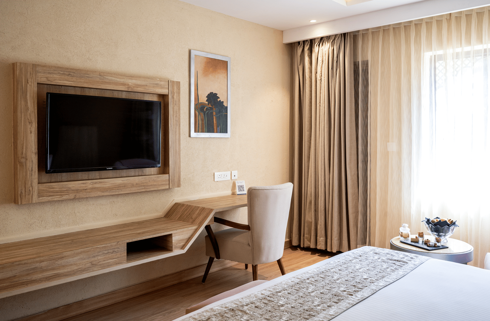 Standard Room at Essentia Luxury Resort & Spa, Udaipur featuring a bed facing the TV on the wall over a running work desk with a chair facing the wall near the window