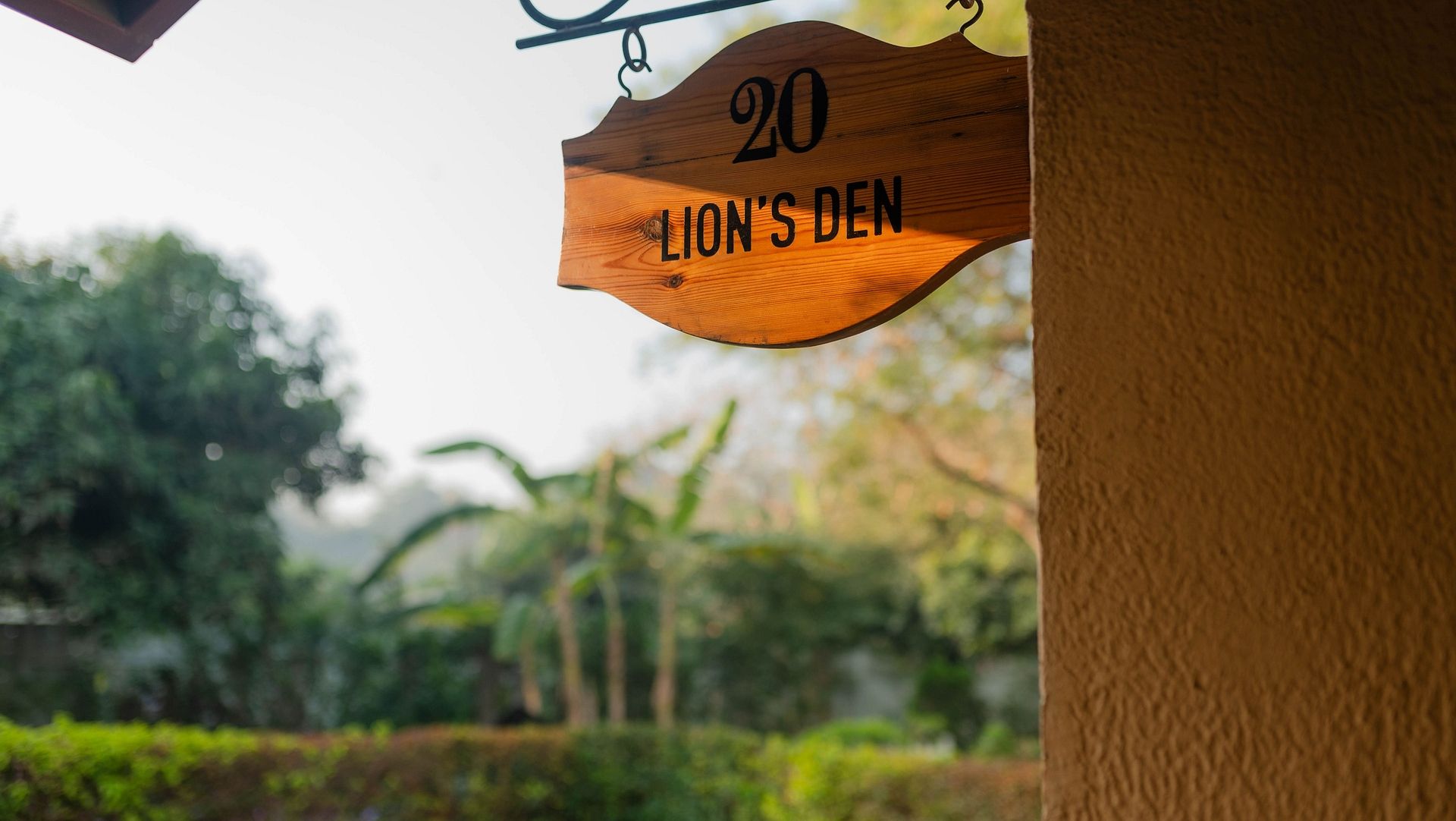 A wooden sign reading Lion's Den 20 hanging outside a unit surrounded by greenery at Karma Chalets.