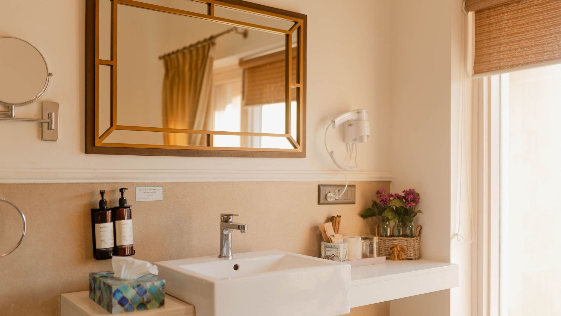 A bathroom at Karma Chalets with a white sink, mirror, toiletries, and a towel rack by the door.