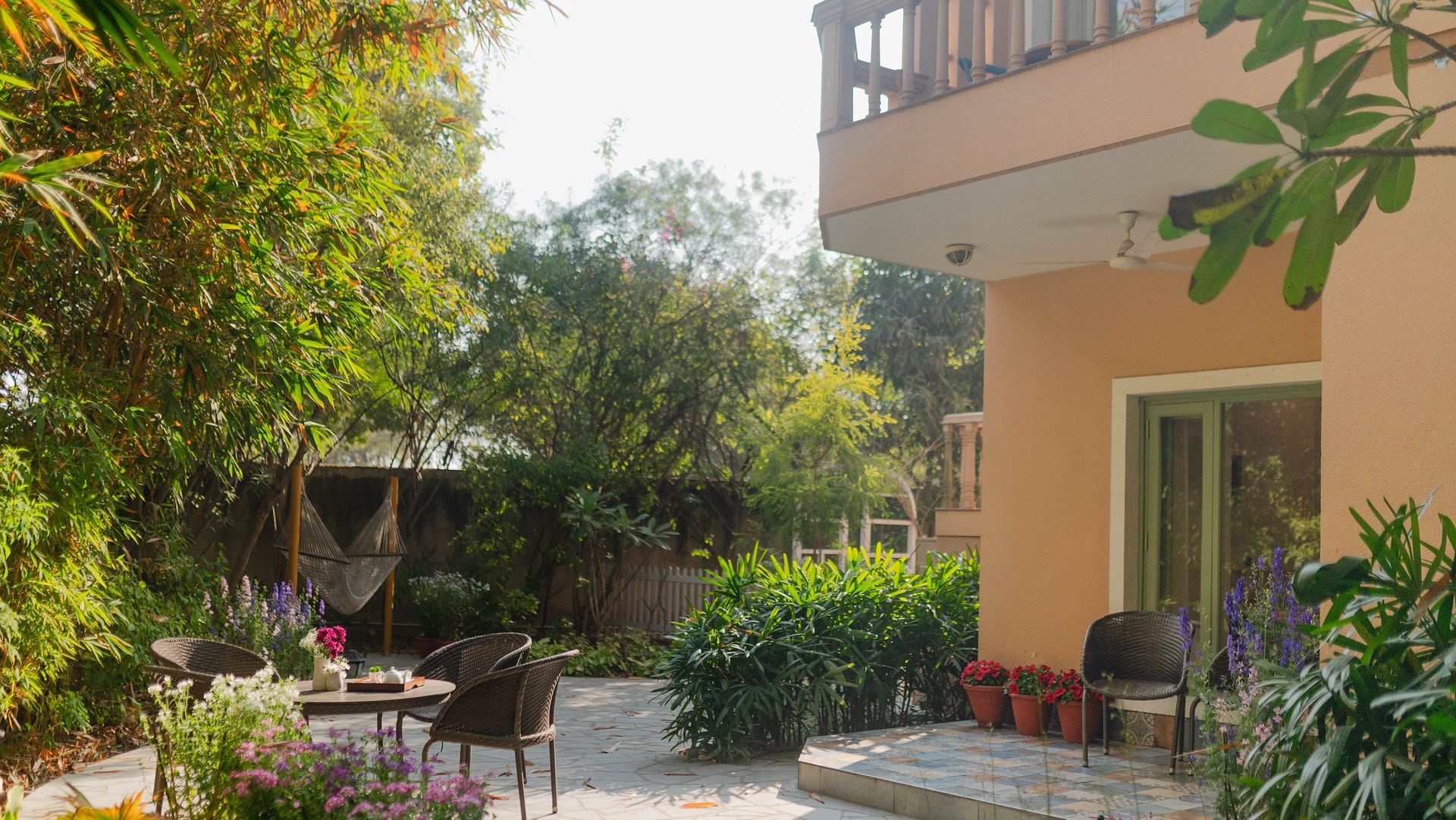 A garden view at Karma Chalets with patio chairs, table, and surrounding plants beside a building.