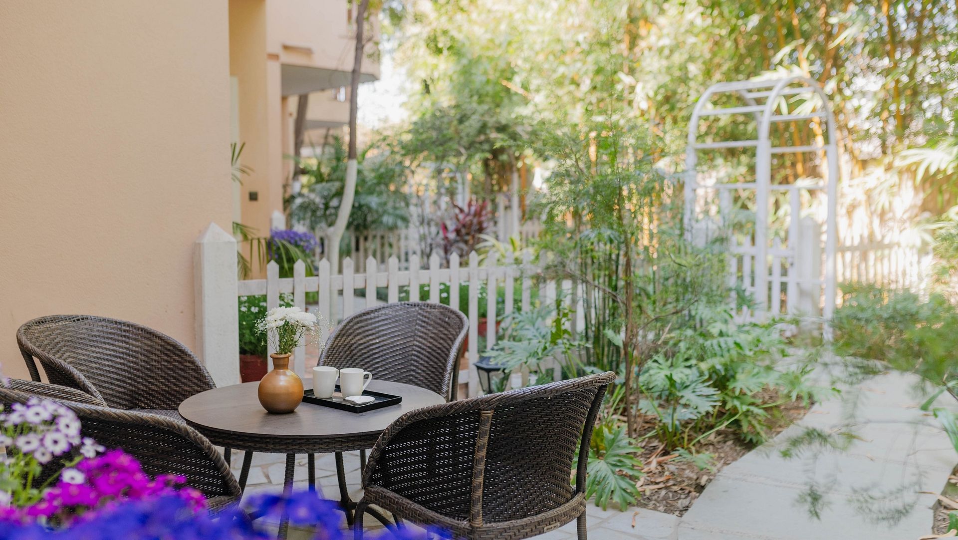 Outdoor seating at Karma Chalets with two black chairs, a table, flowers, and a white gate in the background.