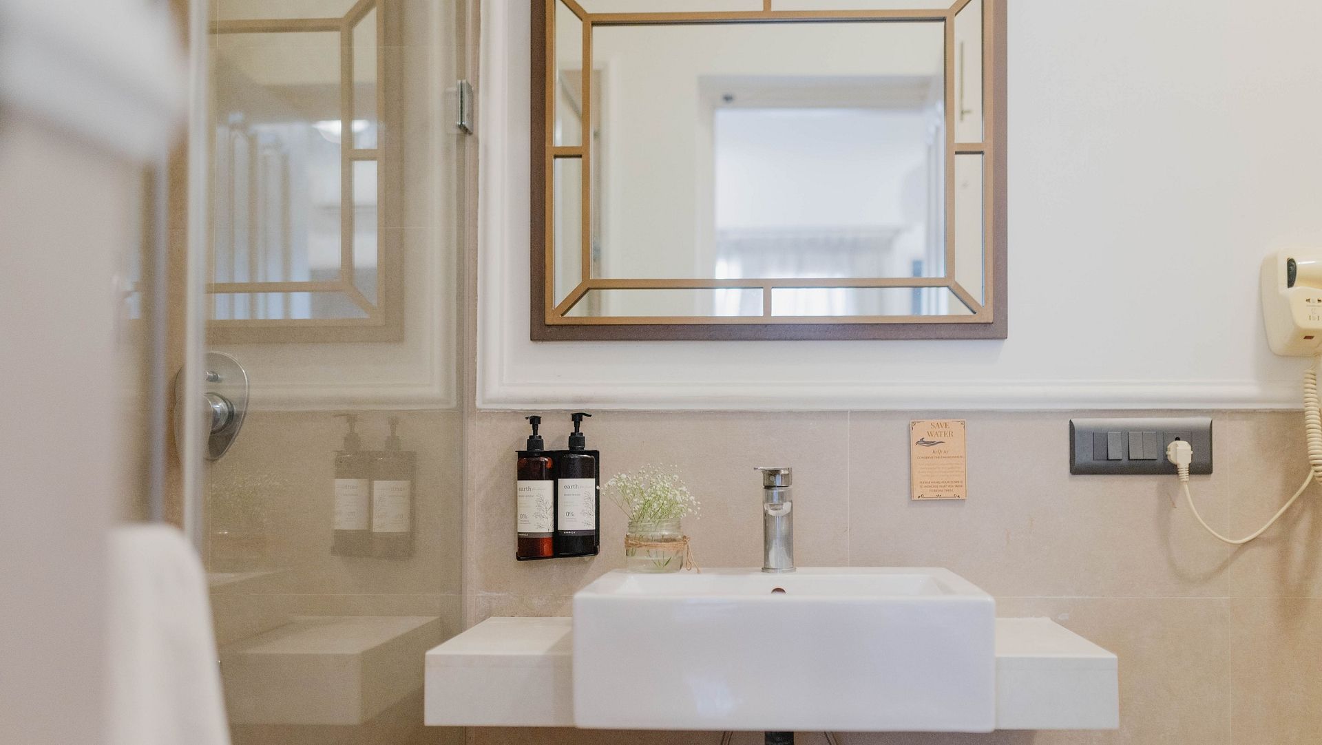 A bathroom at Karma Chalets with a white sink, mirror, soap dispensers, and grey-tiled walls.