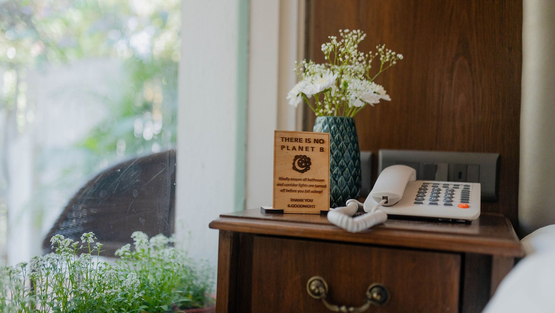 A close-up of a nightstand at Karma Chalets with a telephone, books, and potted plants.