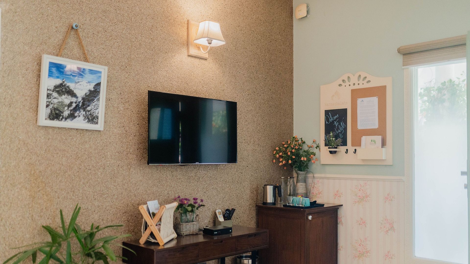 A view of a wall-mounted TV, desk, mirror, and plants in a room at Karma Chalets.