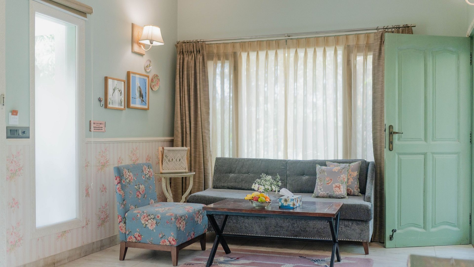 A sitting area at Karma Chalets with a grey sofa, armchair, coffee table, and large window with curtains.