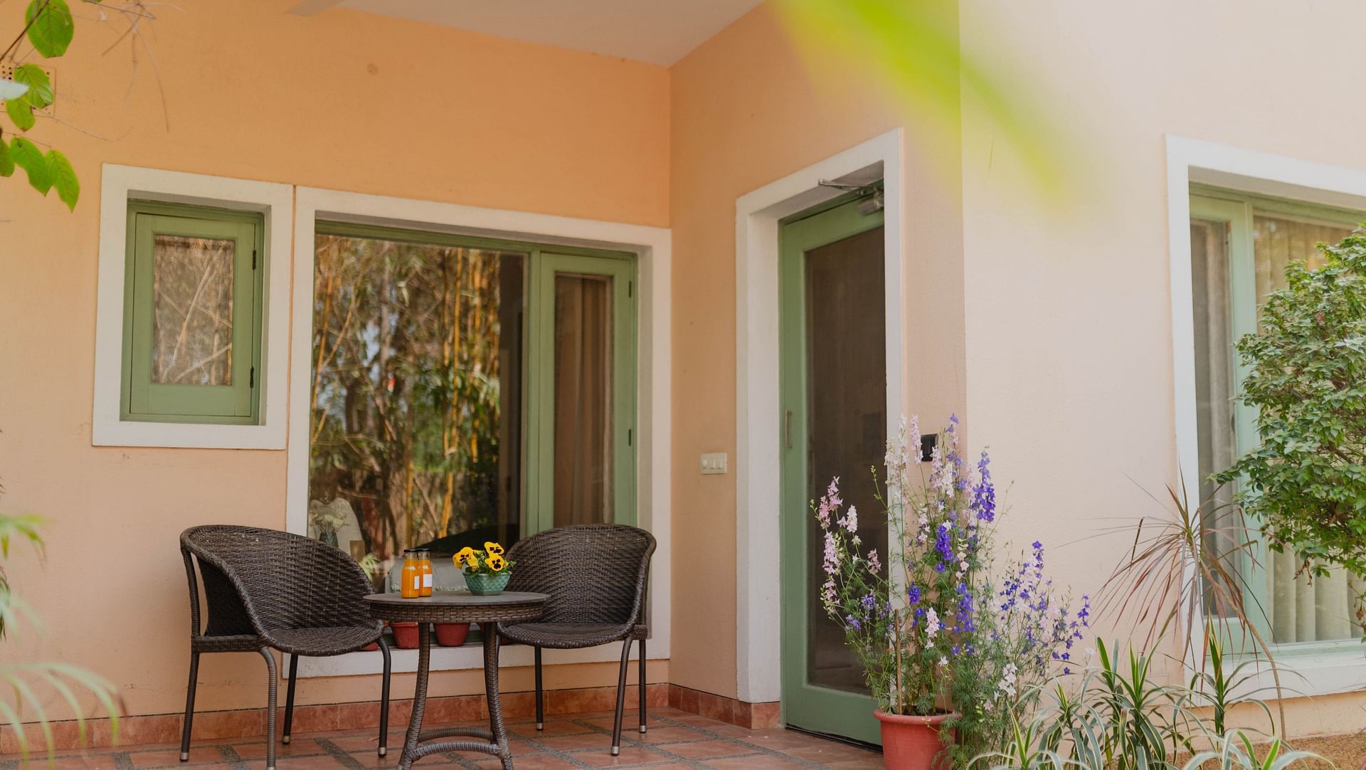 Exterior of a Karma Chalets unit with two chairs and a table on a tiled porch, surrounded by plants.