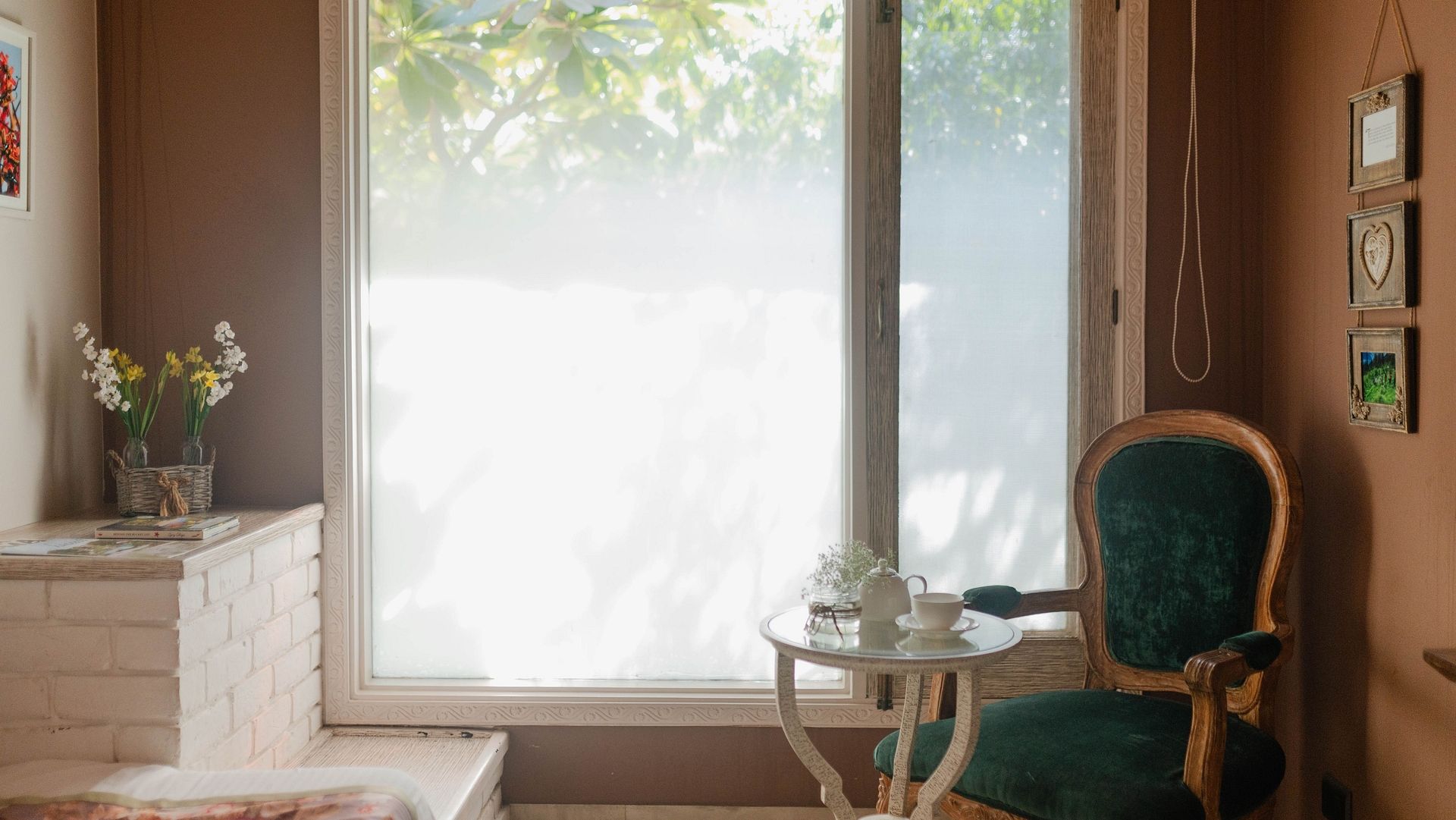 A bedroom at Karma Chalets with a window, green chair, white drawers, and a vase with flowers.