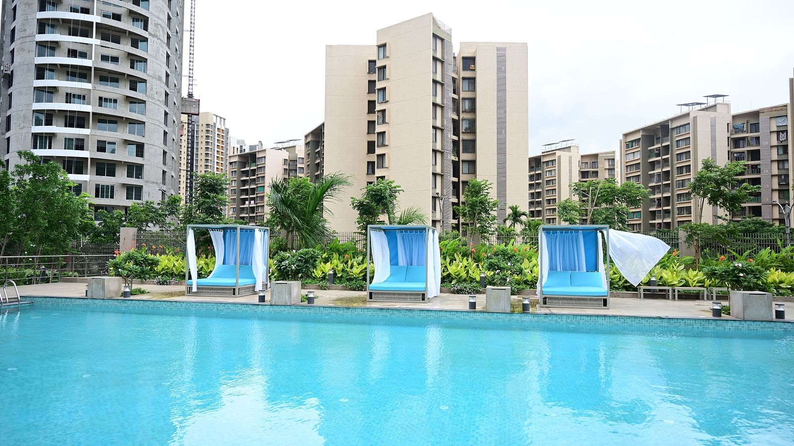 three sun loungers kept on the poolside at club charholi, pune with various buildings in the background