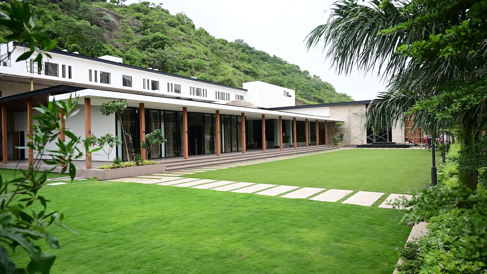 Building with a long porch overlooking a lawn, backed by a wooded hillside.