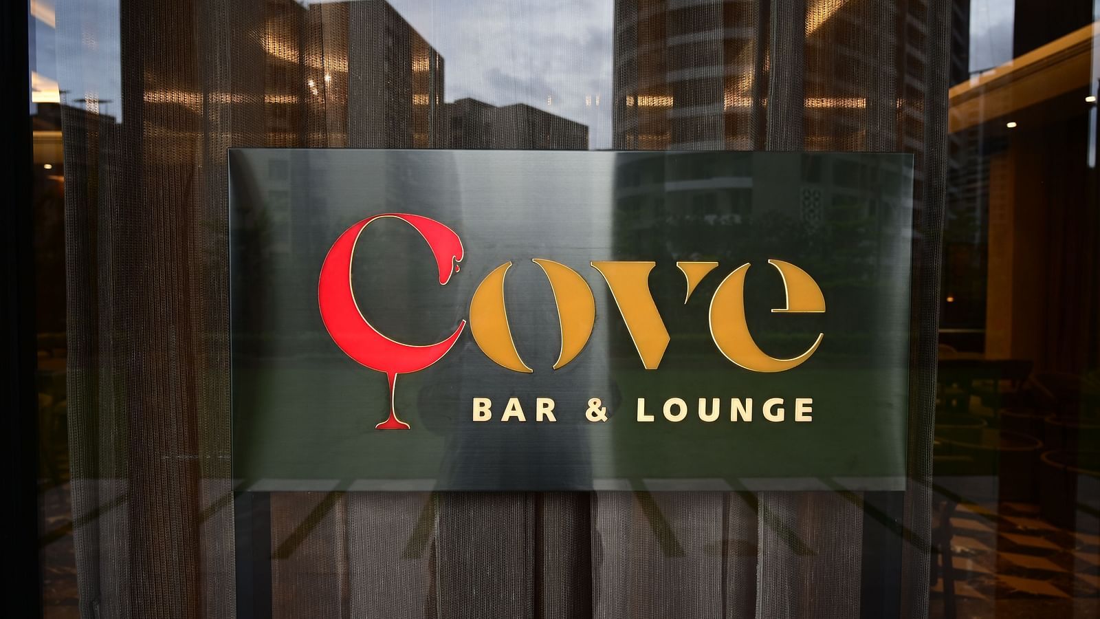 Sign for Cove BAR & LOUNGE with a stylized glass image, seen through a glass door with a city view reflected.