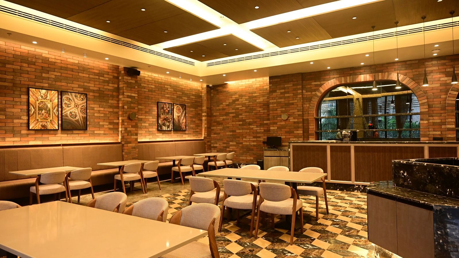 Dining area with tables, chairs, patterned floor, and textured walls, lit by ceiling lights.