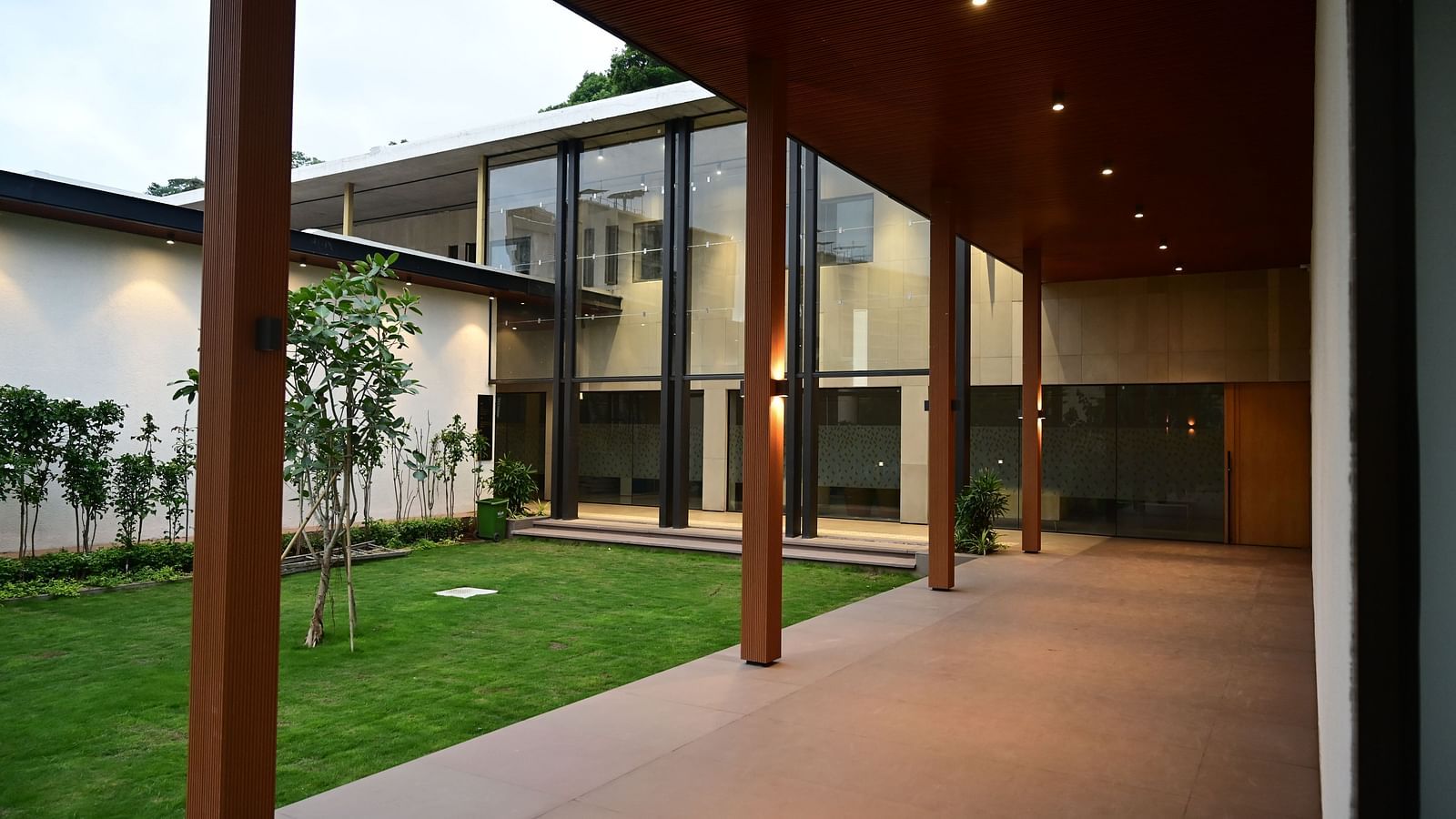 Building with a long porch, glass walls, and a green lawn, viewed from a covered walkway.