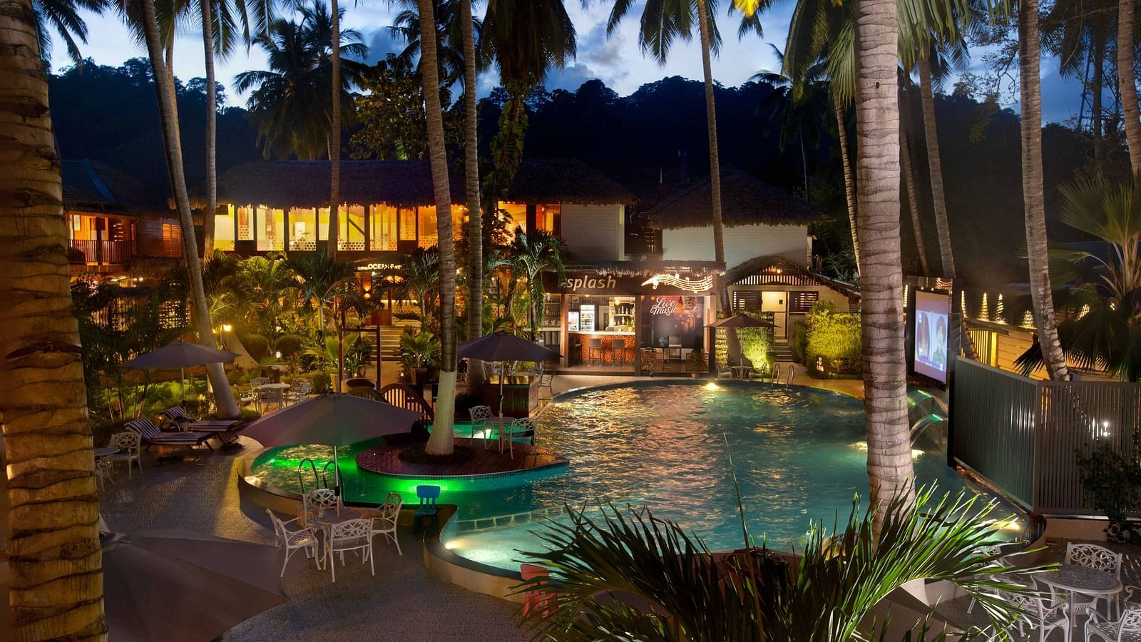  A night-time view of a resort pool area, illuminated by soft lighting. Palm trees surround the pool, creating a tropical and inviting atmosphere - Coral Reef Resort & Spa, Havelock