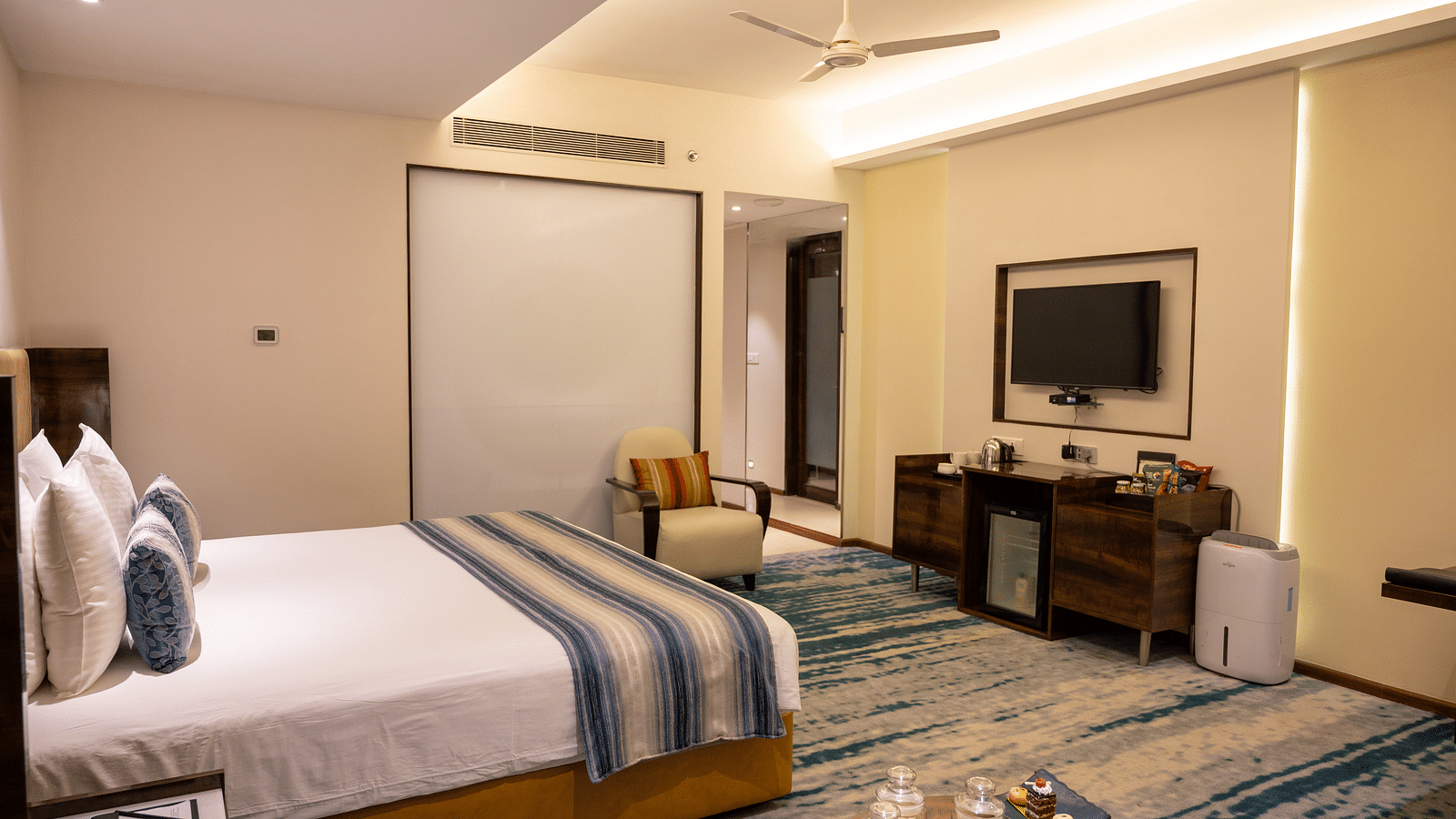 An image of a bedroom with a fan and a wall mounted television at Grand Kakinada by GRT Hotels