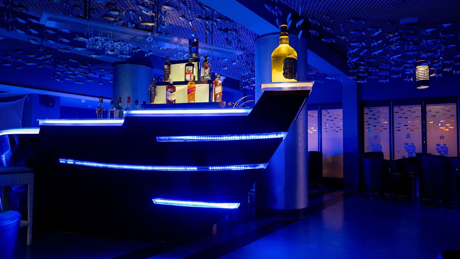An image of ship themed bar with different varieties of liquor  bottles at image of an event hall with tables and chairs at Grand Kakinada by GRT Hotels