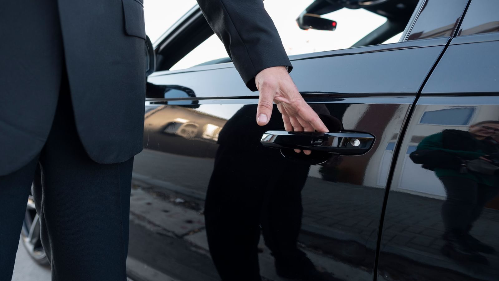 Chauffeur in a black suit opening the door of a sleek black luxury car.