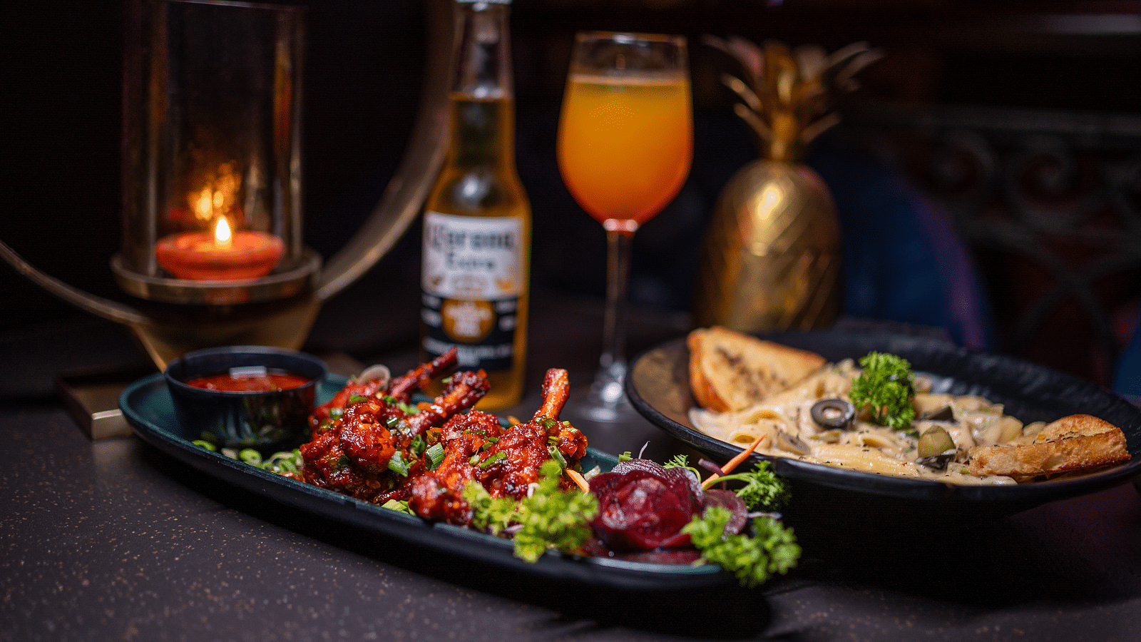 A plate of delicious food accompanied by a beer bottle and a glass of drink, all beautifully arranged with a candle for a cozy atmosphere at hotel moti palace.