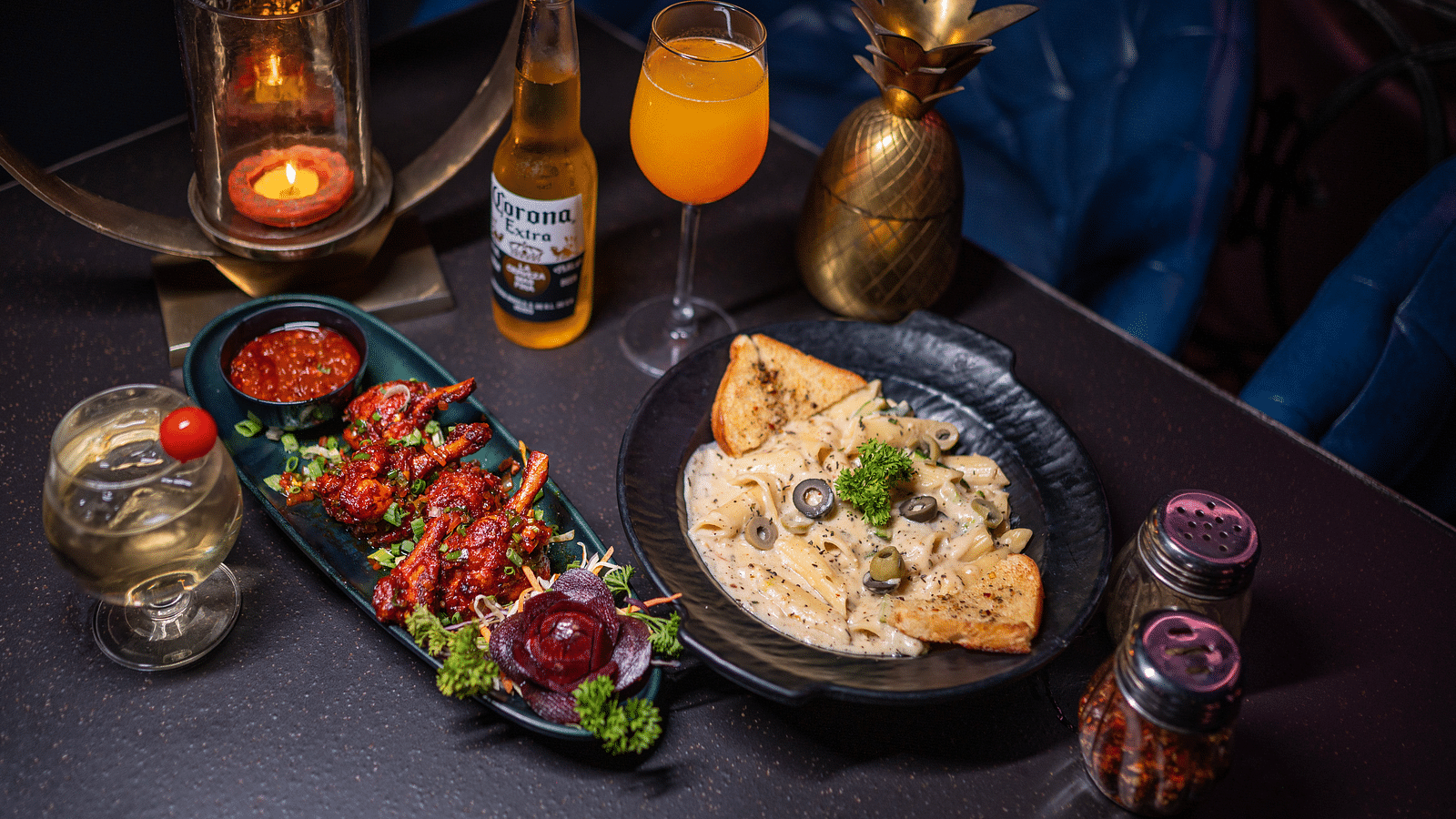 A top-view of dining table with a  plate of delicious food accompanied by a beer bottle and a glass of drink, all beautifully arranged with a candle for a cozy atmosphere at hotel moti palace.