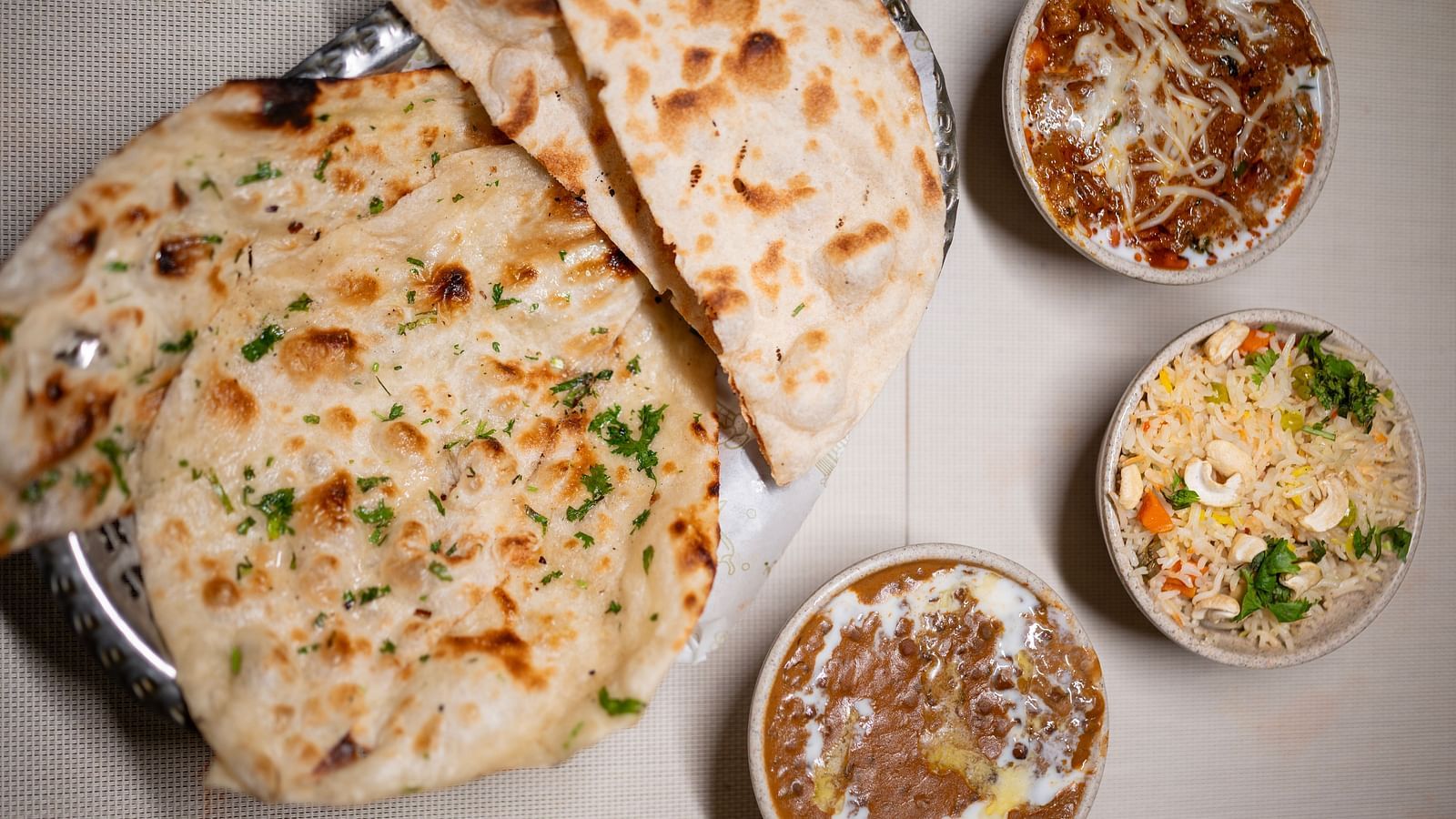 Top view of an Indian meal with naan, bowls of gravy, fried rice, and a sizzling platter of stir-fried veggies Hotel Moti palace ..
