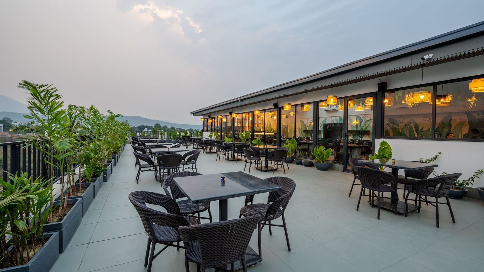 Shot of an outdoor seating area at Vishranti Hotel, Dehradun with a seating area features multiple tables with chairs, and plants are visible in the background.