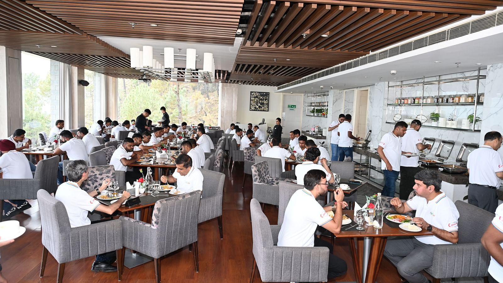 Group of people in white uniforms dining in a modern restaurant with buffet service and large windows - The Zion, Shimla.