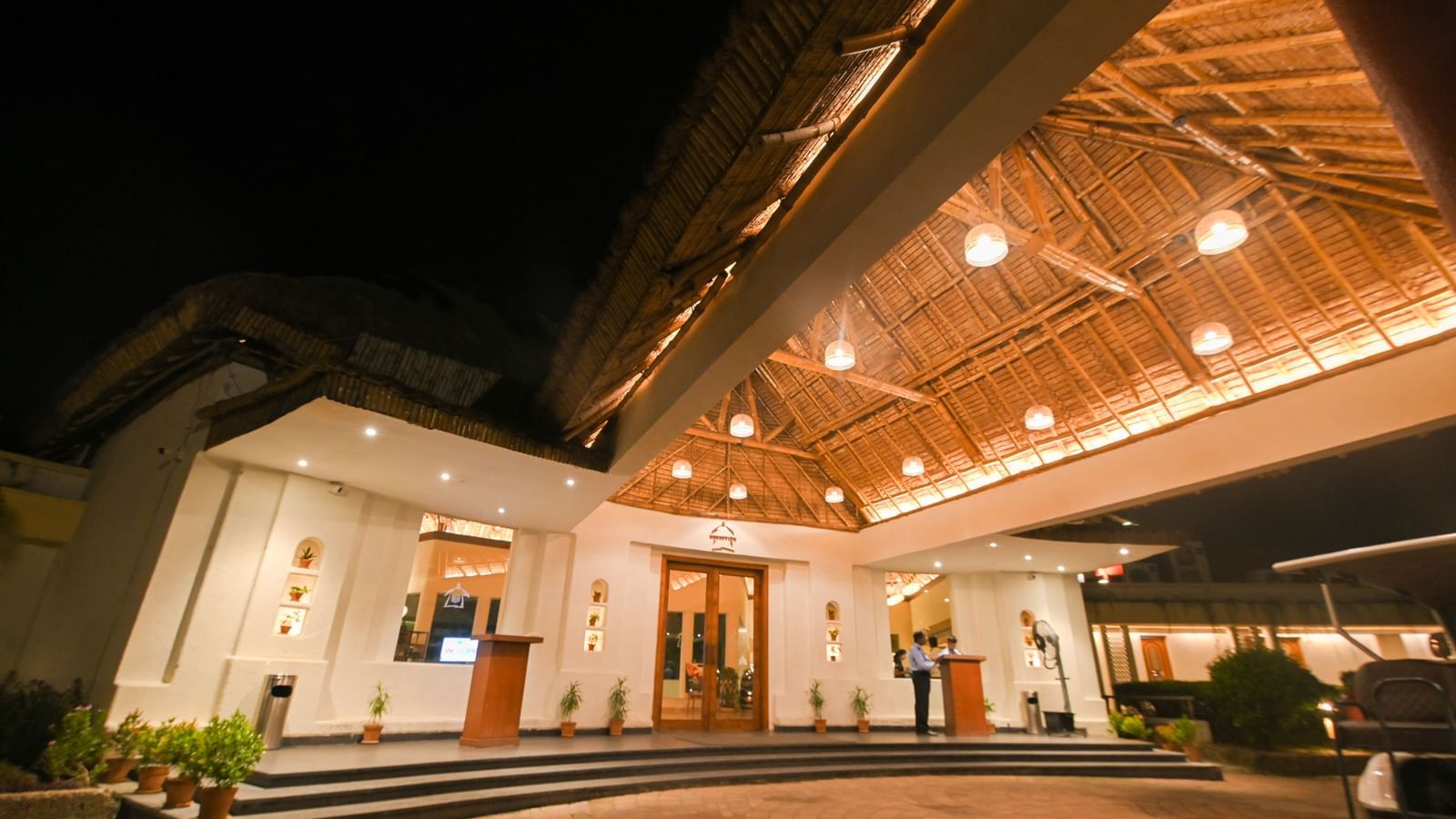 The entrance of Vedic Village Spa Resort featuring an illuminated path way leading to the reception and staff on duty.