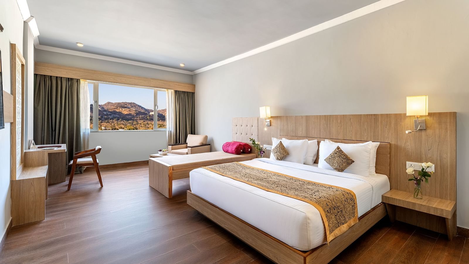 A hotel room with a made bed, side tables, a desk, and a large window with a view - Via Lakhela Resort & Spa, Kumbhalgarh