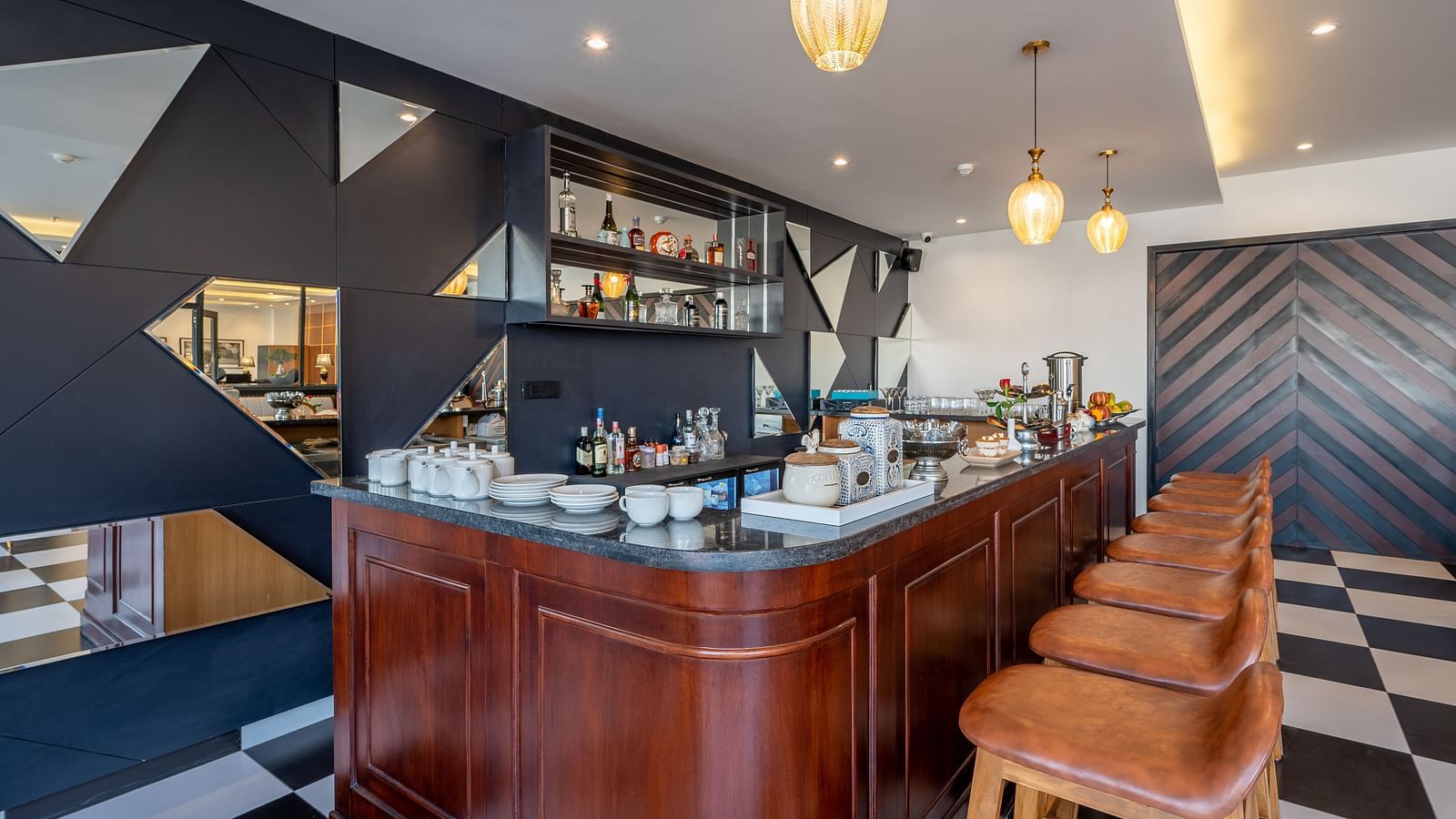 Close up shot of a bar at Vishranti Hotel Dehradun featuring chairs, tables, a bar counter and checkered floors. 