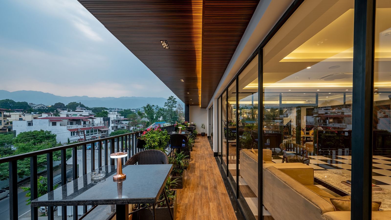 An outdoor dining area on a balcony, of The Spirit Tribe Restaurant at Vishranti Hotel, Dehradun. The balcony features a dark-colored metal railing, a wooden floor, and a dining table with chairs.