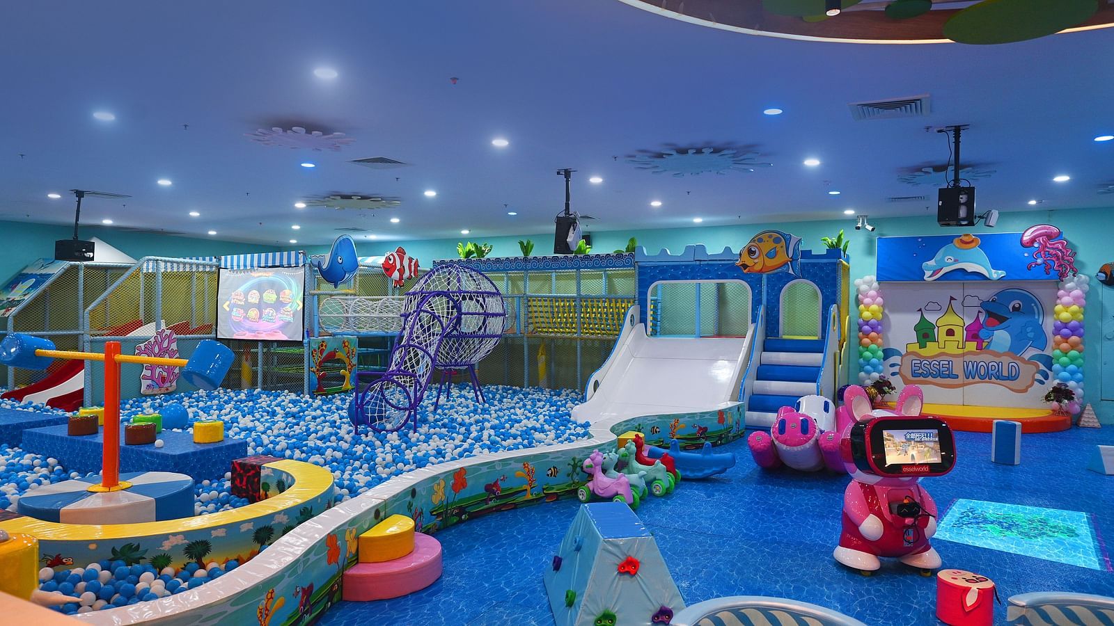 Indoor playground with colorful equipment, slides, and a ball pit, filled with children playing.