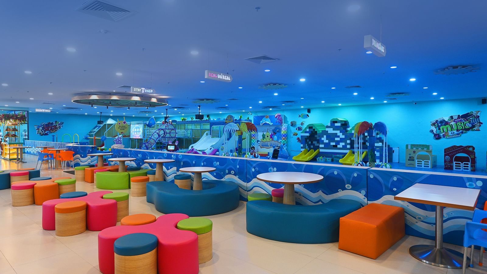 Indoor playground with blue flooring, colorful seating, and various play areas, designed for kids.