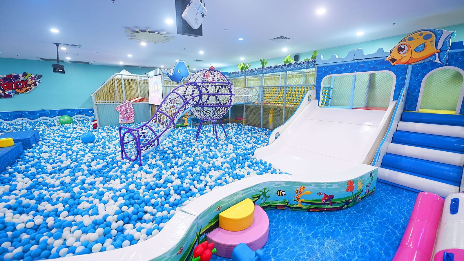 Indoor play area with a large ball pit, slides, and various play structures under bright lights.