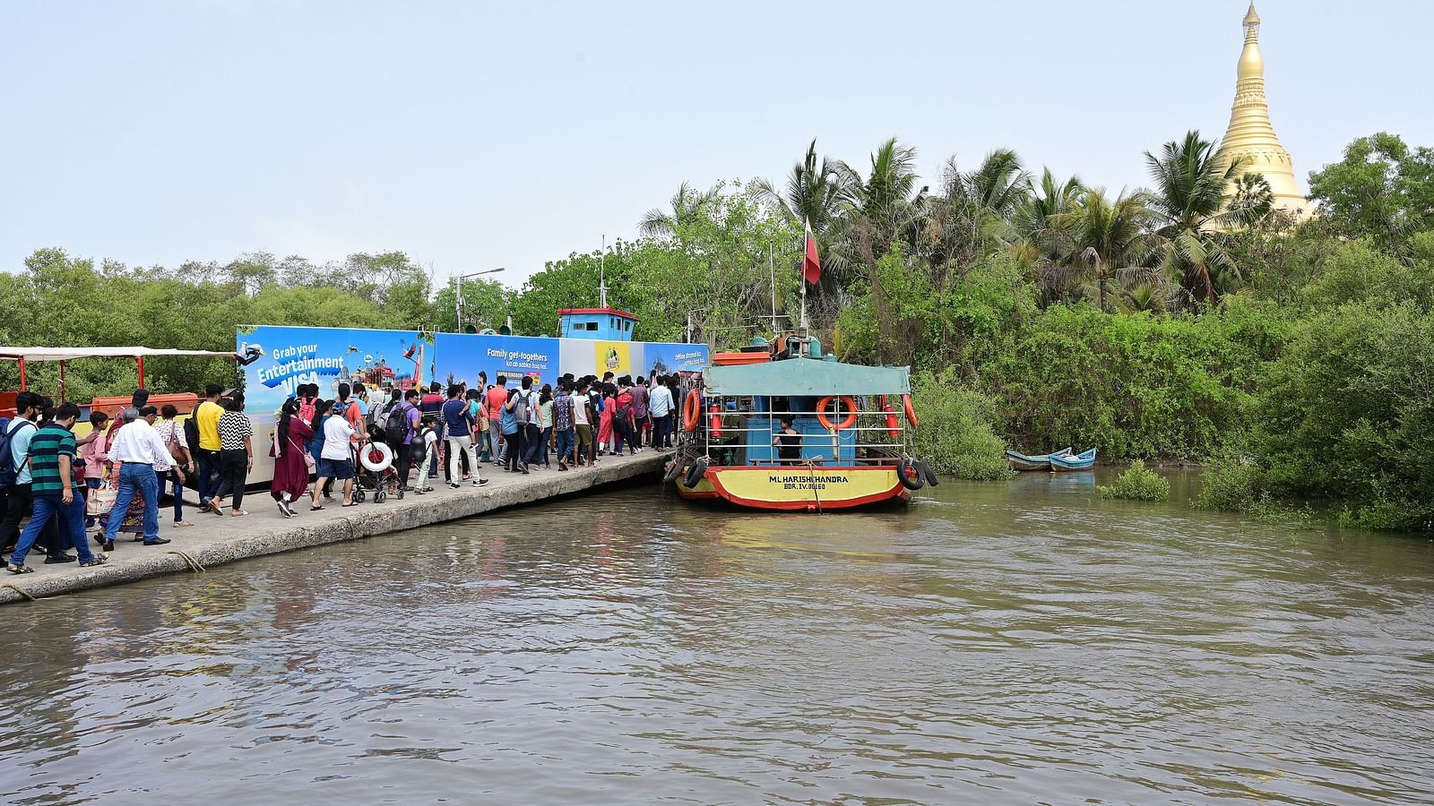 Boat docked on a river with a crowd of people boarding, against a blue sky background.