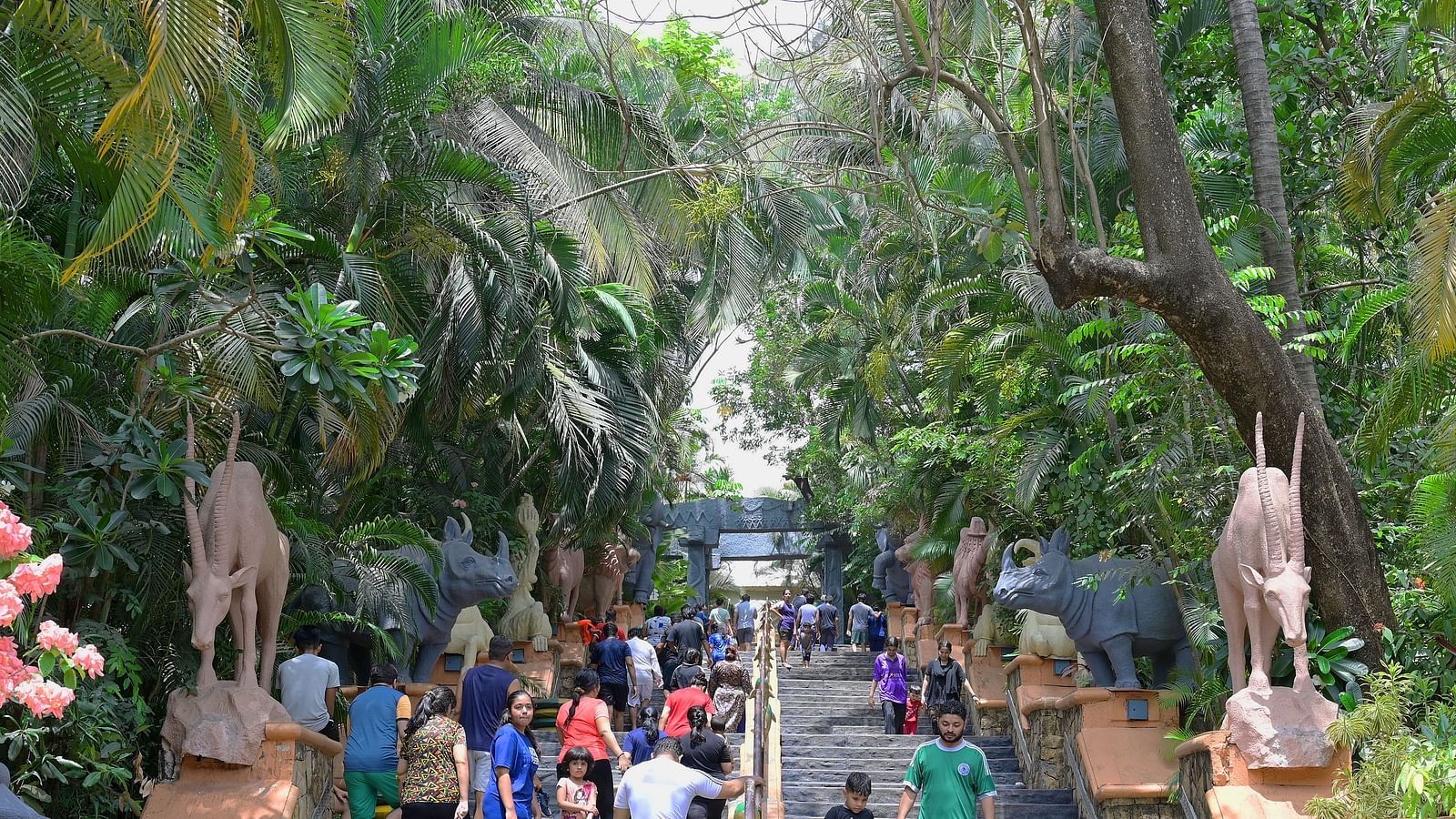 Path lined with tall trees and people walking through a lush, green park.