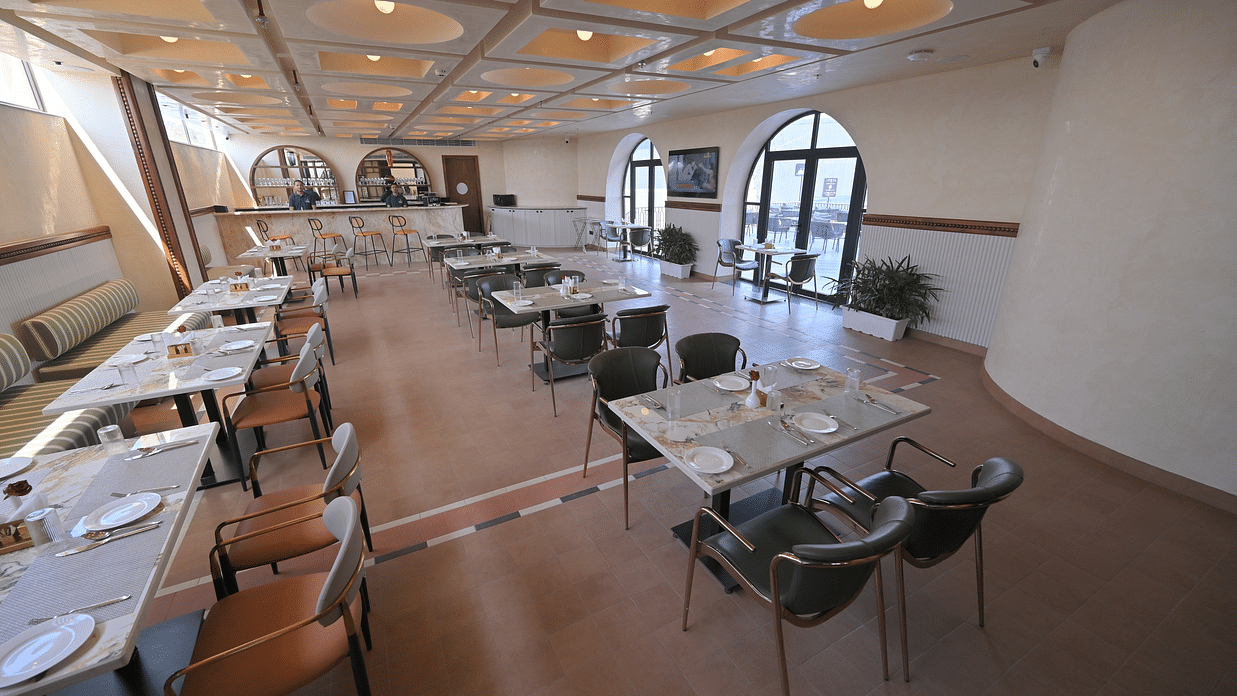An interior of a restaurant with tables set for dining and large windows. - Clarks Safari Haridwar